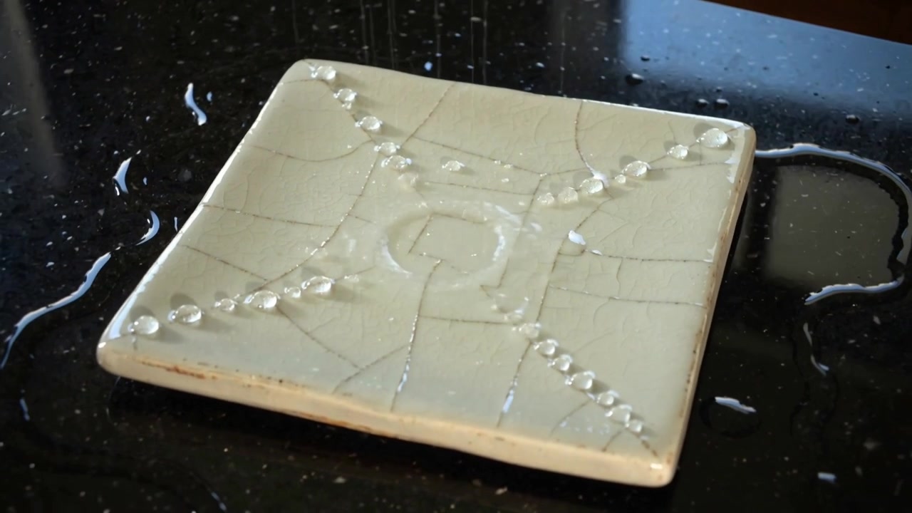 Forming ceramic tile drawing bead chains on crackle glaze on stone counter, with pool touching edge