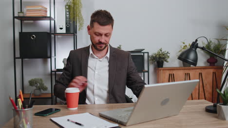 Businessman-enters-office-start-working-on-laptop-computer-at-desk-and-drinking-morning-coffee