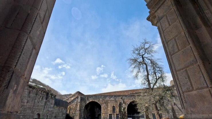 Un arco si erge imponente, incorniciato da un cielo azzurro limpido e nuvole soffici. Dietro l'arco sono visibili degli alberi. La gente cammina nelle vicinanze a San Miguel de Allende durante il giorno.
