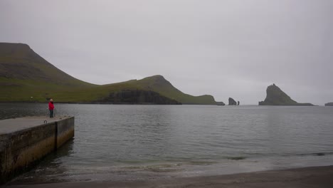 woman looking at the horizon to drangarnir sea stacks and tindholmur and turning back to the camera