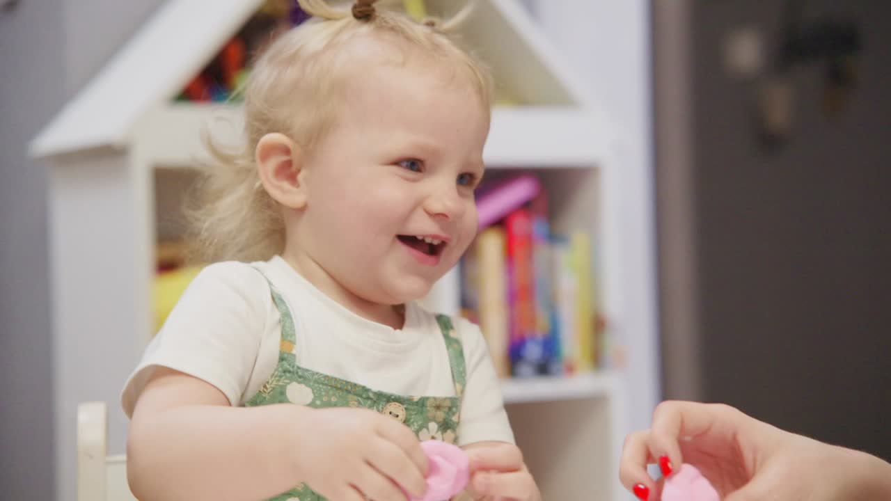 Bambina piccola felice che gioca con la plastilina rosa in casa
