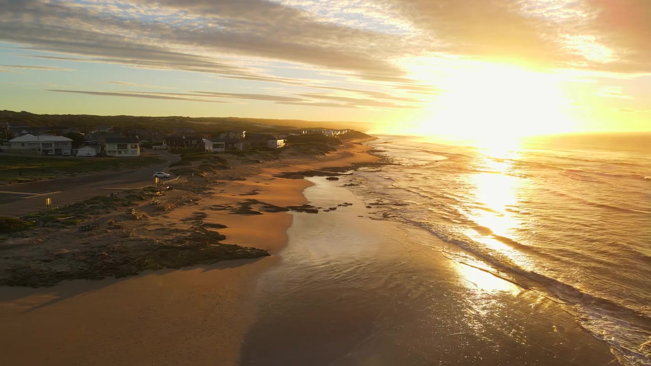 Levende solopgang over havet, mens bølger slår ind mod kysten ved kystbyen Witsand på Sydafrikas Garden Route. Luftsporing
