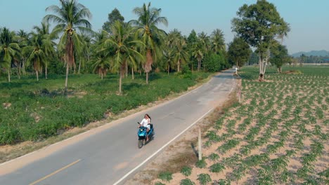 girl-rides-scooter-along-road-at-tropical-site-upper-view