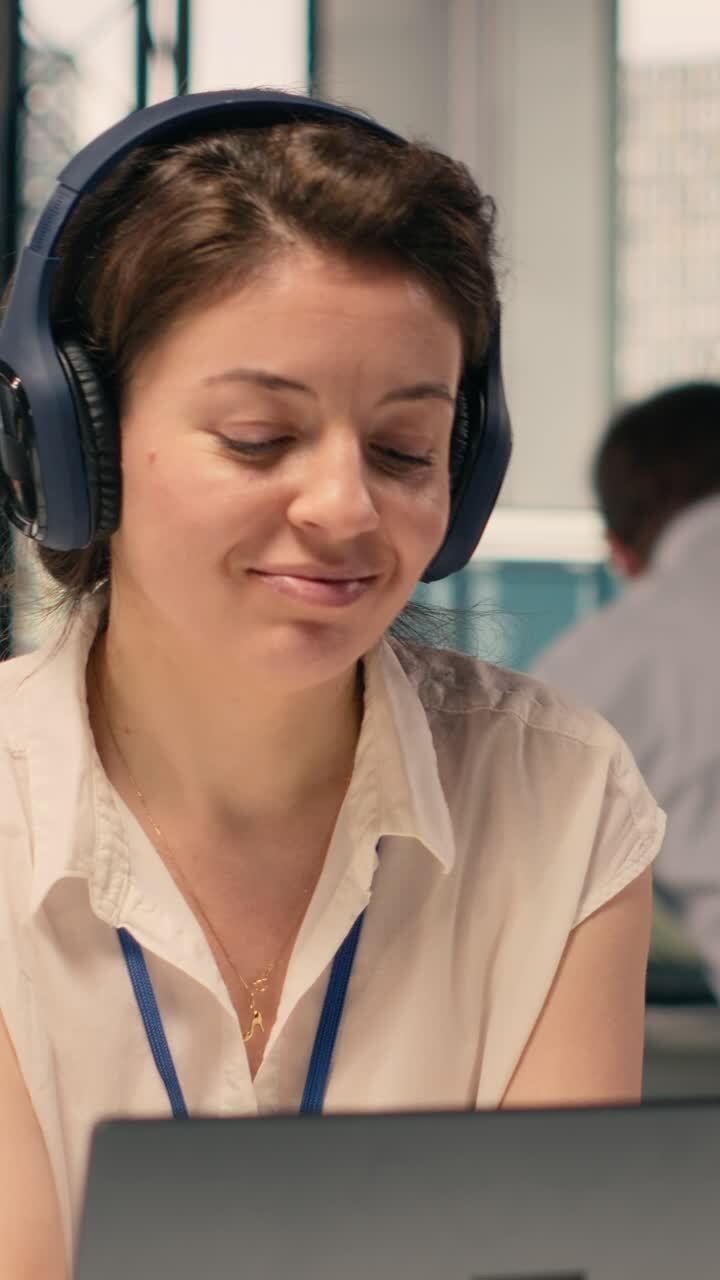 Žena si nasazuje sluchátka a s úsměvem pracuje na notebooku