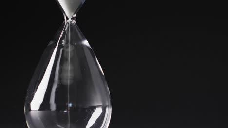 Video-of-close-up-of-hourglass-with-sand-pouring,-copy-space-on-black-background