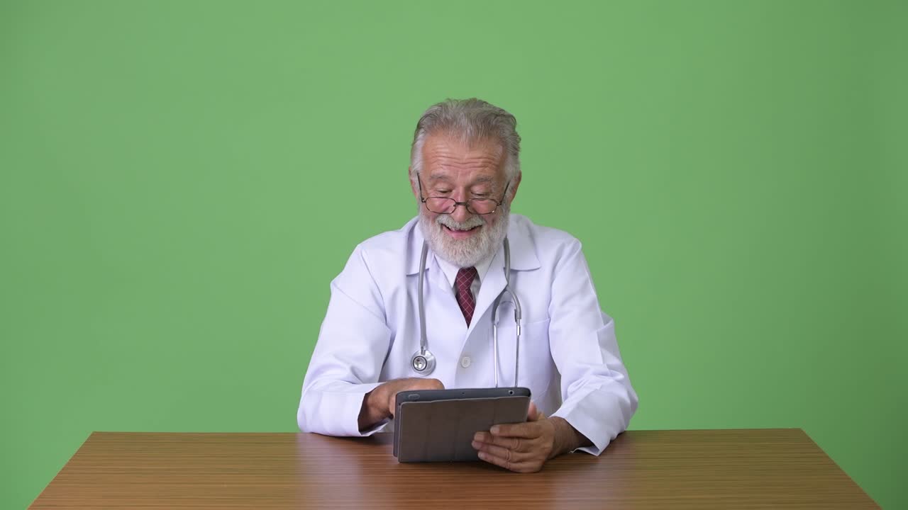 Medico anziano affascinante con la barba su sfondo verde.