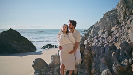 una pareja embarazada y linda abrazándose de pie en una playa soleada. una pareja feliz esperando a un bebé