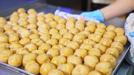 brown baked balls of future desserts being pulled out of oven. big baking sheet covered with profitroles. confectionary concept.