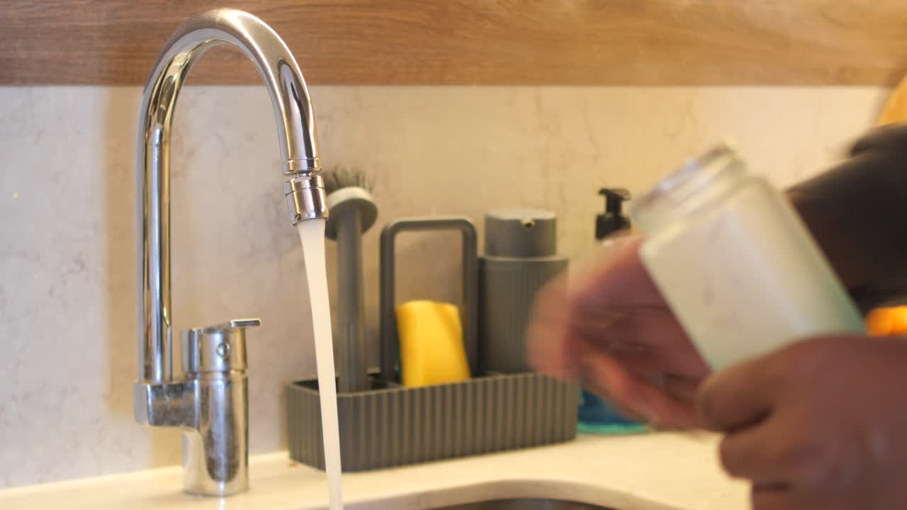 una persona llena una botella de agua con agua de un grifo del fregadero de la cocina