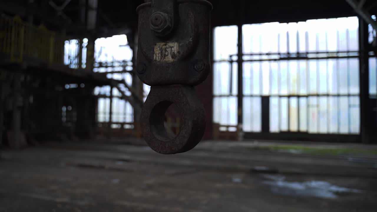 Old rusty hook hanging in an abandoned spooky scary industrial factory slightly moving at daylight