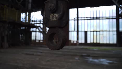 old rusty hook hanging in an abandoned spooky scary industrial factory slightly moving at daylight