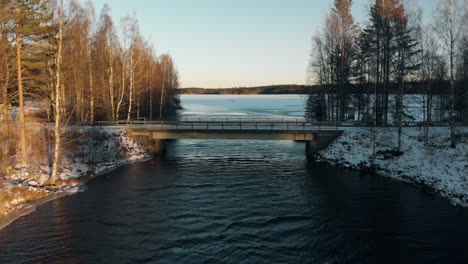 aérien, tir de drone, au-dessus d'une rivière, au-dessus d'un pont, vers un lac, entouré d'une forêt sans feuilles et de la première neige au sol, par une journée d'hiver ensoleillée, près de joensuu, carélie du nord, finlande