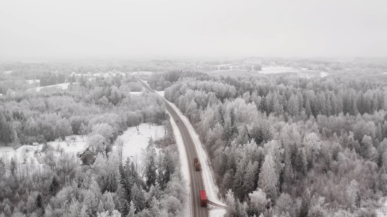 Aerial drone view of cars and trucks driving on a snowy highway through a frozen winter landscape with icy trees. Two lane asphalt road in countryside. Hoar frost on trees.