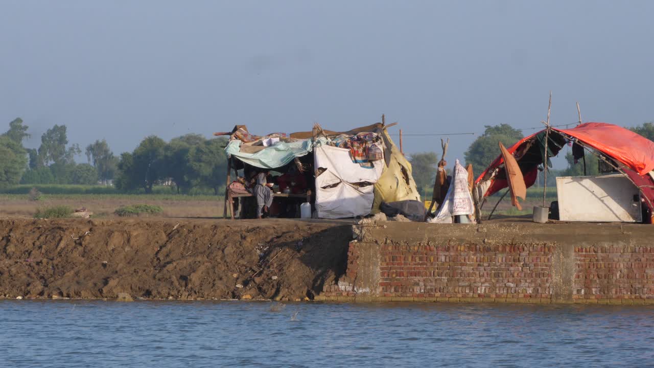 toma de campamentos improvisados al fondo con agua de inundación fluyendo en el frente en sindh, pakistán, en un día soleado.