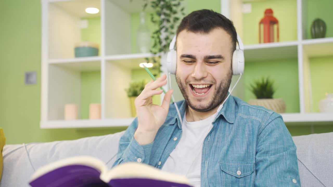 un joven tranquilo y relajado leyendo un libro escuchando música en casa.