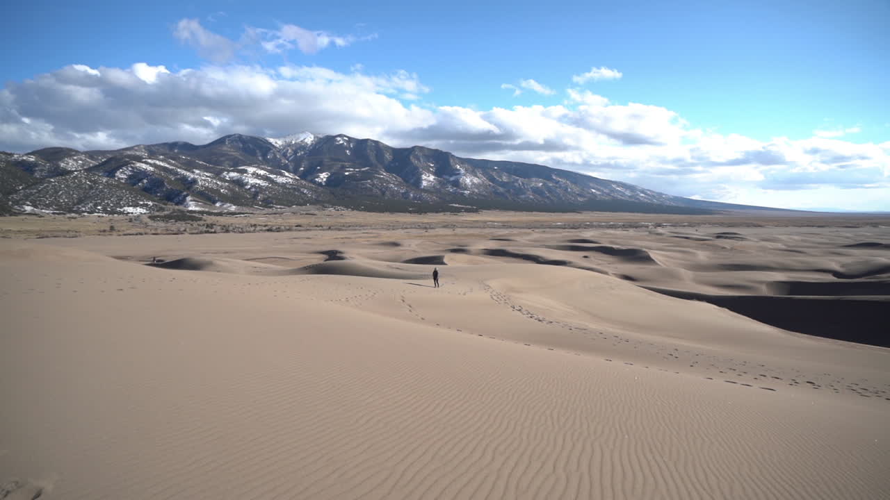 눈 덮인 산 언덕을 배경으로 모래 언덕을 걷고 있는 외로운 사람