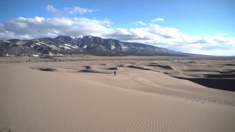 one lonely person walking on dune with snow capped mountain hills in background