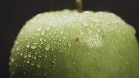 Micro-video-of-close-up-of-green-apple-and-water-drops-with-copy-space-on-black-background