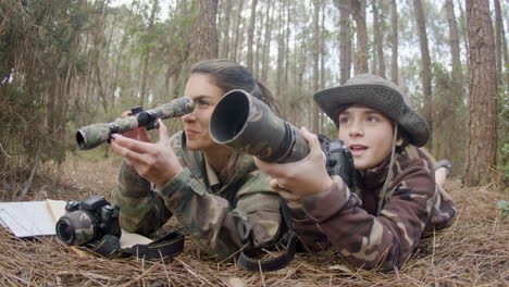 mulher feliz e seu filho observando pássaros deitados no chão da floresta