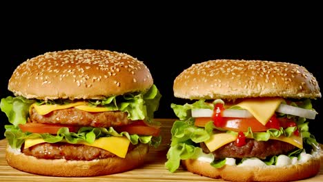 close-up of two appetizing burgers with sesame buns rotating on black background, of fast food seamless looping shot