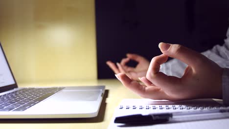 young female hands doing yoga on a minimal office workplace with a laptop, a notebook and a pen, for stress relief during work