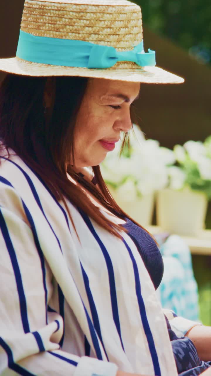 A Woman in a Stylish Straw Hat with a Blue Ribbon: Enjoying a Relaxing Moment Outdoors Surrounded by Lush Greenery and Blossoming Plants