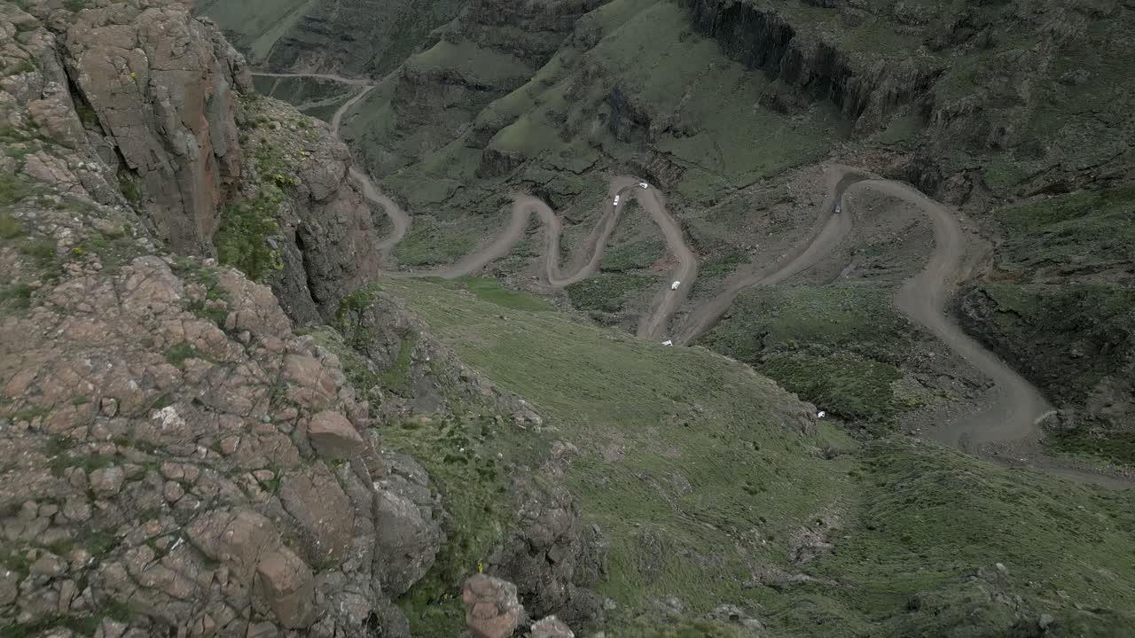 revelación aérea: vehículos en la carretera de sani pass de zigzag de grava, lesotho