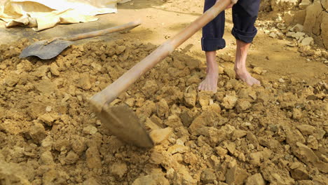 the sun shines on a barefoot man breaking clay soil, showing the hard work and dedication of sourcing pottery