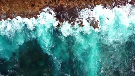 Vista-Estática-Aérea-De-Las-Fuertes-Olas-De-Aguas-Prístinas-Contra-Las-Rocas-En-Las-Costas-De-Curacao,-Una-Isla-Caribeña-Holandesa