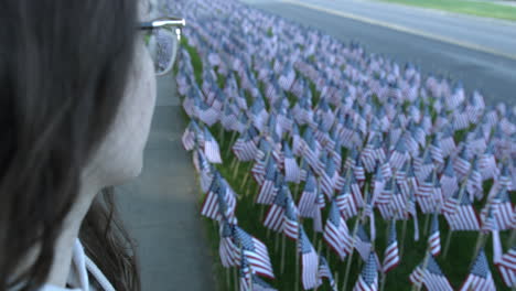 extreme close up of a woman in eyeglasses staring on a lot of american flags at the park