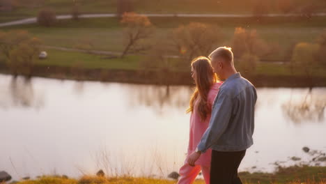 happy young people walking in nature at sunset. beautiful girl and blond guy holding hands and walk near the river in the evening.