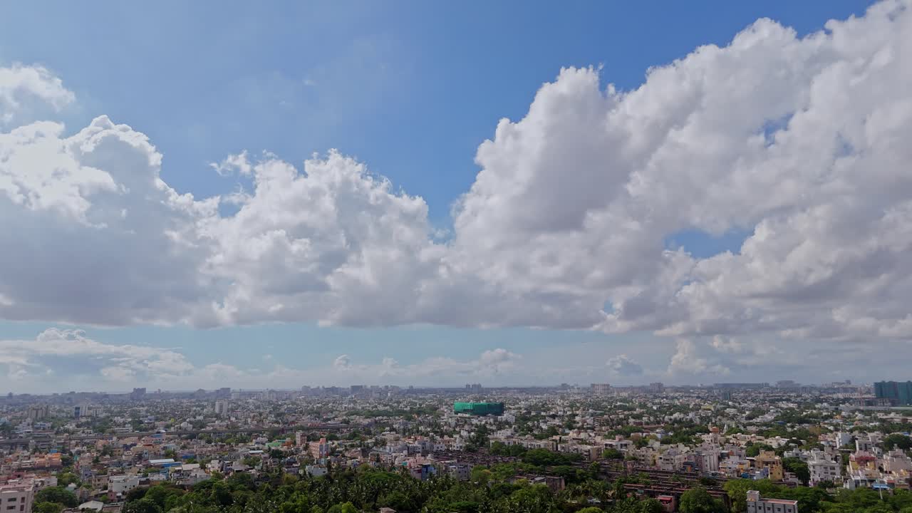 Aerial shot featuring cityscape with large, fluffy cumlus clouds in sky during daytime.