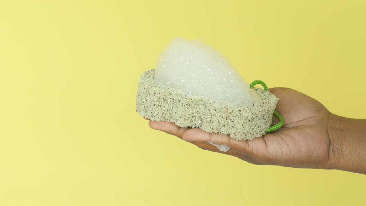Hand holding a natural sponge with soap bubbles