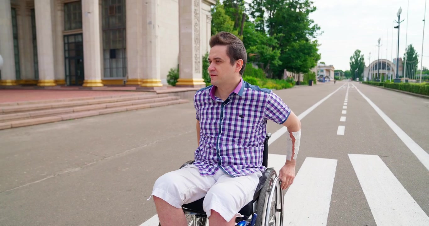 Young Man in Wheelchair Moving Along a Road in a Park