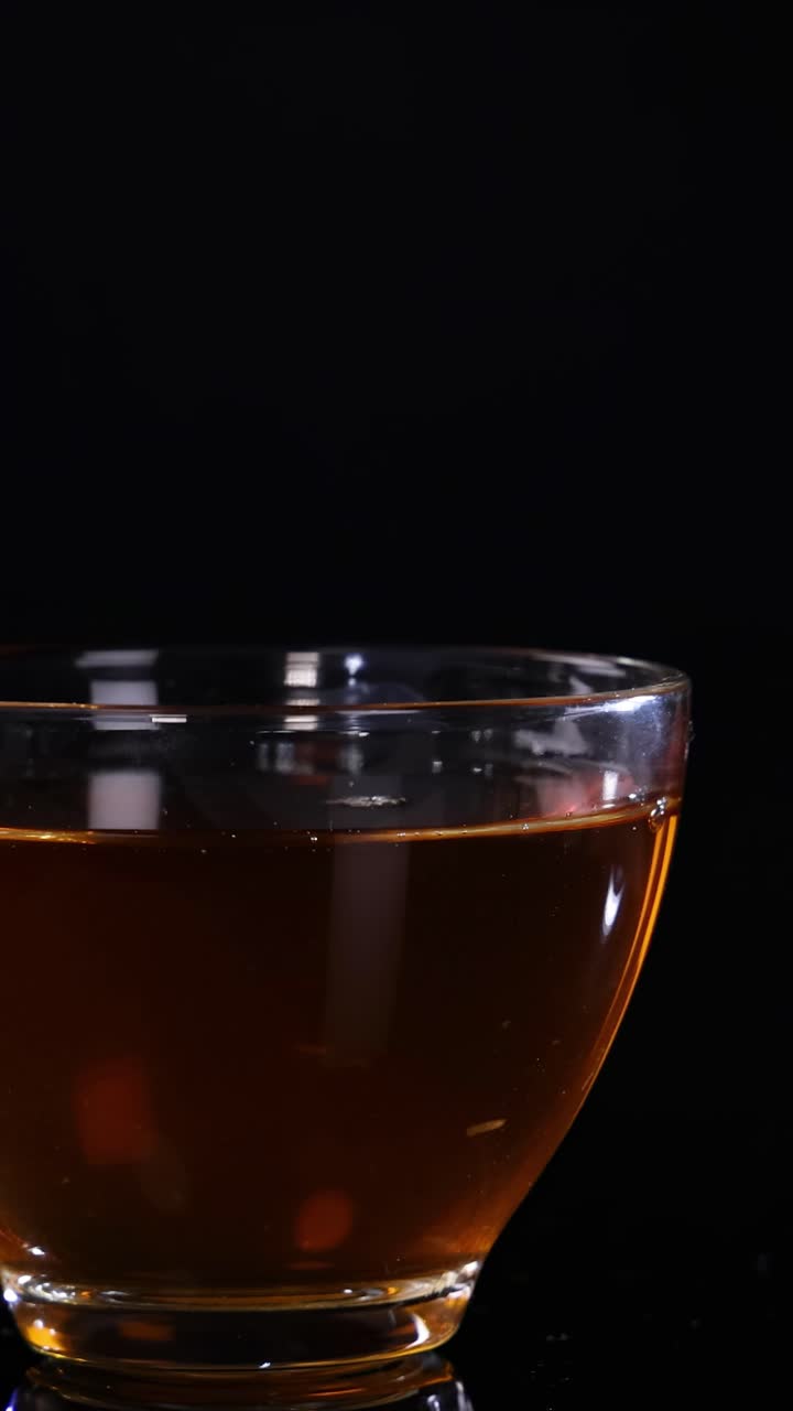 Una tazza di vetro piena di tè poggia su uno sfondo nero, mettendo in mostra un'illuminazione sottile e riflessi.