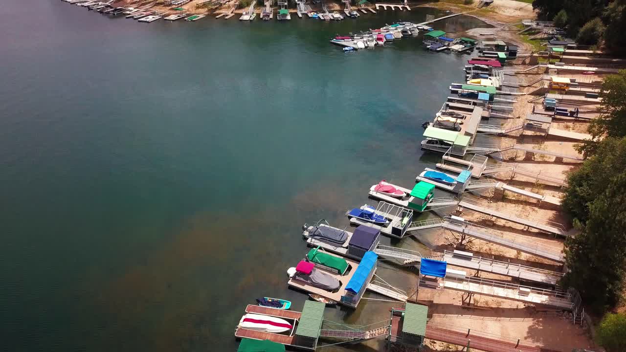 Aerial flyover boat docks lining the shoreline of a lake in the mountains. 4K