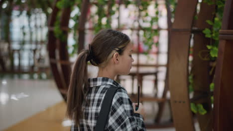 vista trasera de una joven con cabello brasileño caminando en una zona de asientos bellamente decorada, ella lleva una mochila negra en un moderno espacio comercial interior con muebles elegantes