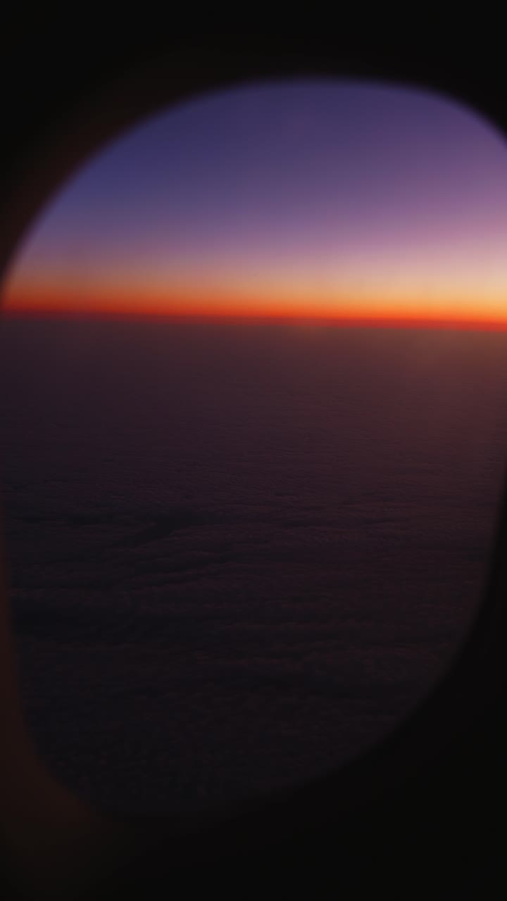 Cinematic sunset view captured from an airplane window during flight, featuring warm golden light illuminating a vast cloudscape at cruising altitude