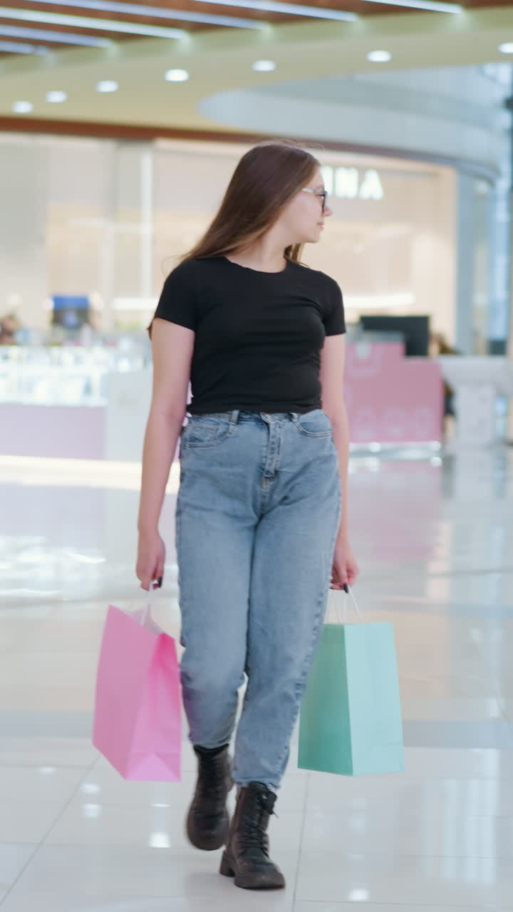 활기찬 쇼핑몰에서 쇼핑백을 들고 돌아다니며 호기심을 불러일으키며 걸어가는 학생, 다른 쇼핑객들이 지나가며 바쁜 쇼핑 센터 분위기를 보여줍니다.