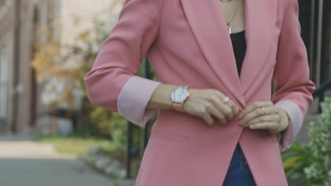 caucasian lady wearing black top buttoned up her pink jacket suit while walking on a sunny day