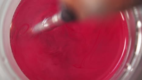 vista de arriba hacia abajo de la pintura roja liberándose y extendiéndose a través del agua por el remolino del pincel