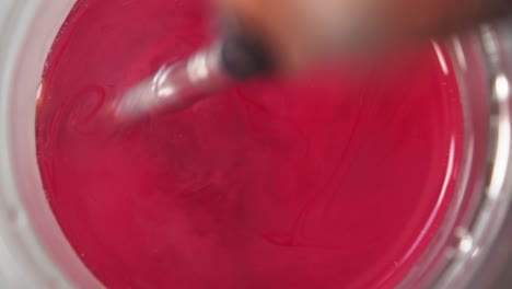 top down view of red paint releasing and spreading across water from brush swirling