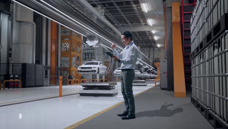 vista lateral completa del cuerpo de un trabajador profesional masculino asiático de pie con su tableta en la fábrica de automóviles ev, instalación industrial de alta tecnología, levanta el puño con un objetivo gritador