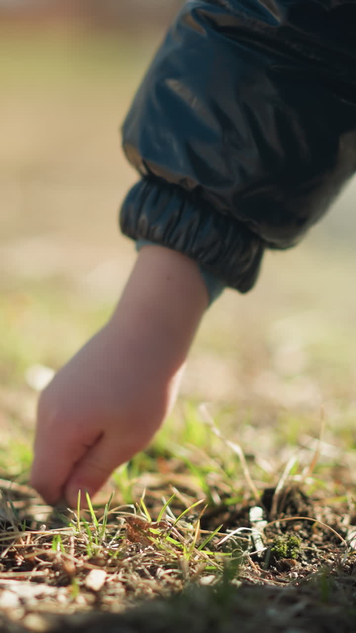 la mano de un niño joven, con una chaqueta de cuero, vaqueros y botas, mientras recoge un palo para cavar en el suelo, el palo se rompe, y después de intentarlo de nuevo, lo arroja en ira