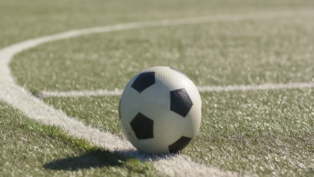 En sort-hvid fodbold ruller fra højre kant langs en hvid bue og sænker farten på grund af friktionen mod græsset