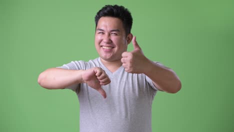 young handsome overweight asian man against green background