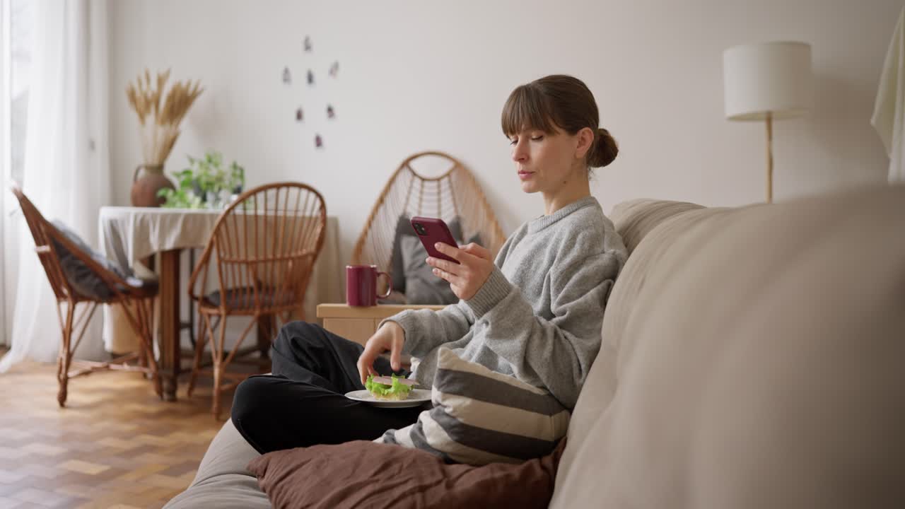 Woman relaxing on couch with phone and sandwich
