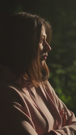 pensive young woman breathes heavily in fresh forest air while standing under light of street lamp. lonely female person in warm coat feels sad while relaxing in nature