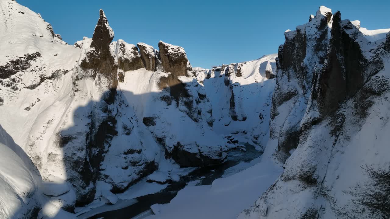 vista aérea a través de un cañón cubierto de nieve, sobre un río glaciar que fluye, en un día soleado