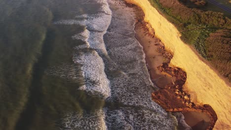 slow motion orbiting of the cliffs at beautiful sunset in a panoramic view with the water waves moving too and fro touching the sand in acantilados de mar del plata, argentina